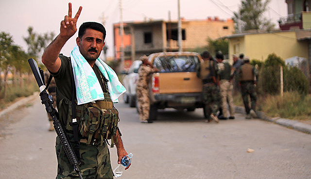 A Kurdish fighter shows the victory sign after re-capturing the town of Tel Asquf from ISIS militants.