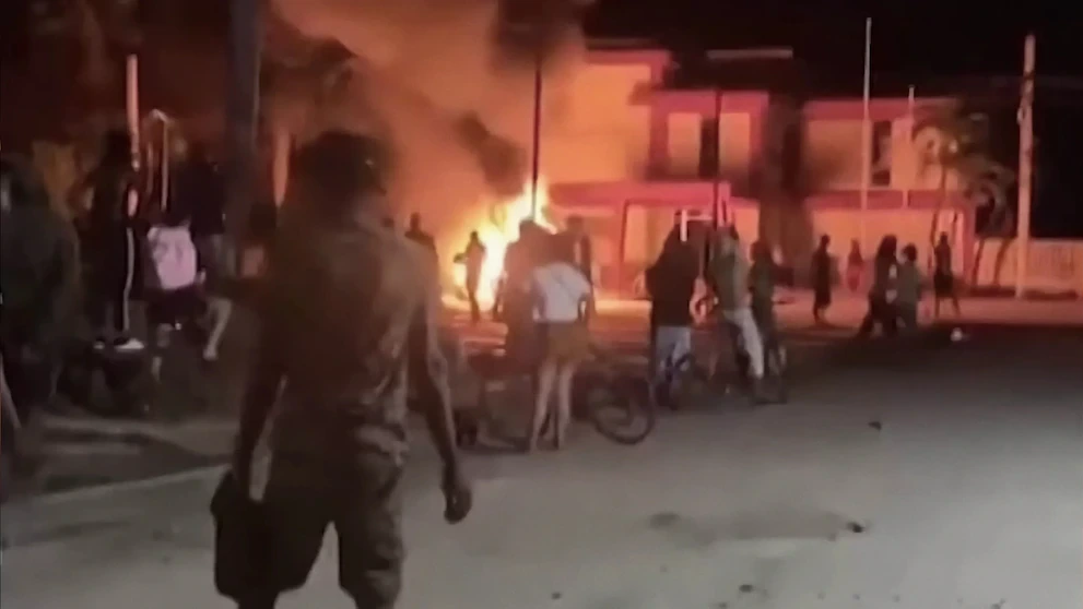 Manifestantes cubanos observan la sede del partido comunista de una localidad incendiada