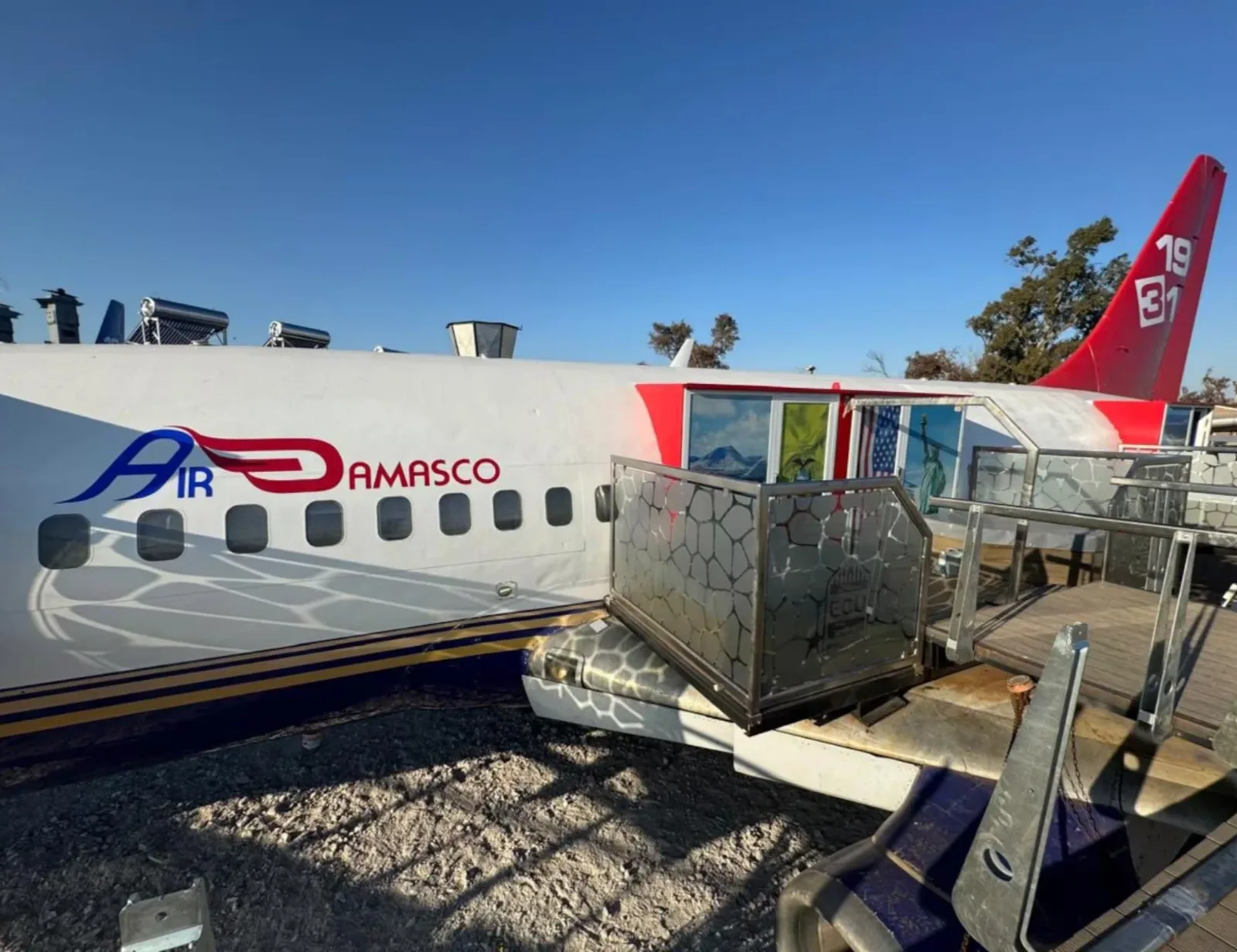 Uno de los aviones del hotel, con el logo de Air Damasco y la cola roja con el número 1931. El acceso a las habitaciones se hace por pasarelas de madera.